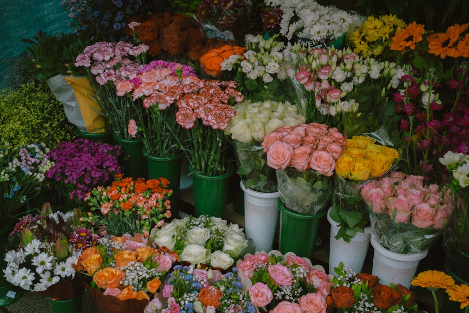 A vibrant display of fresh floral arrangements at a florist shop, featuring a variety of flowers including pink, white, yellow, and orange roses, daisies, statice, and carnations, arranged in green va