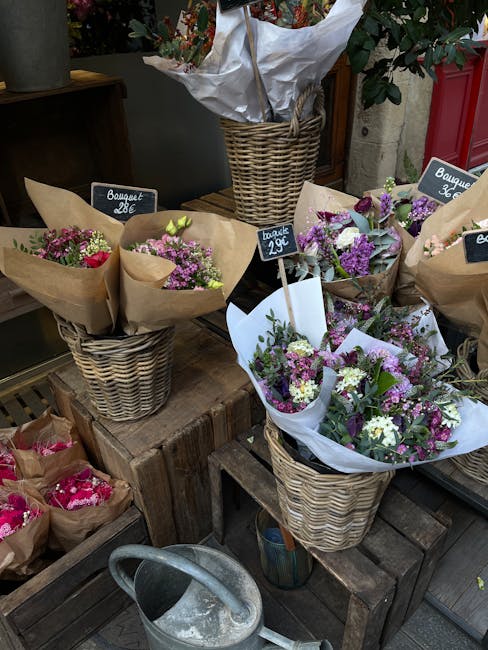 An arrangement of fresh flower bouquets displayed in woven wicker baskets at a flower shop, with a variety of purple, white, and pink flowers including lisianthus, chrysanthemums, and filler blooms, w