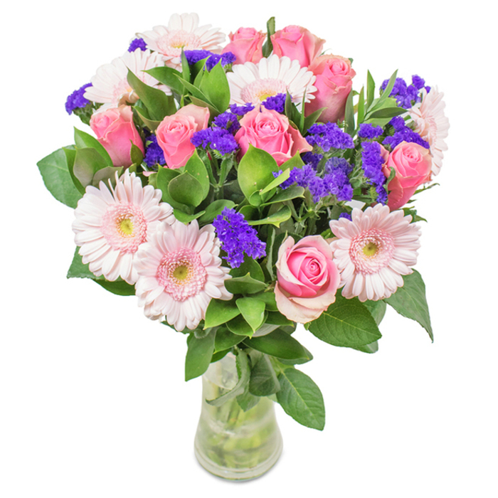 An elegant, eye-catching bouquet stands against a clean backdrop in the heart of Yiewsley. Seven to nine classic pink roses, most just unfurling and some still tightly wrapped, display their spiral charm, nestled with five to seven pale pink gerbera daisies. These daisies, with their broad, gently radiating petals and subtle, nearly white centres, offset the roses beautifully. Threaded throughout are bold clusters of purple statice, providing texture and a pop of deep colour reminiscent of the vibrant florals often seen near Yiewsley Station. A nest of lush, deep green foliage grounds this arrangement, echoing the freshness of the nearby Harmondsworth Moor. Presented in a clear vase, every stem visible through crystal water, this bouquet is ideal for delivery throughout Yiewsley-an uplifting gift for birthdays, anniversaries, Mother's Day, or to adorn local homes and offices with its message of warmth and celebration, reflecting the local florist's deep-rooted pride in quality and artistry.